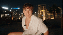 a young man in a white shirt is smiling in front of a city at night