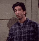 a man in a plaid shirt is making a funny face while standing next to a wall .
