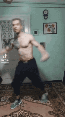 a man without a shirt is dancing in a living room with a clock on the wall above him that says tik tok