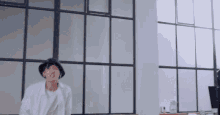 a man wearing a hat is dancing in a room with a lot of windows .