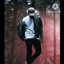 a man wearing a hat and a bomber jacket is standing in a forest