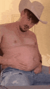 a man wearing a cowboy hat is holding his belly .