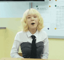 a girl with blonde hair and a white shirt and tie is sitting at a desk