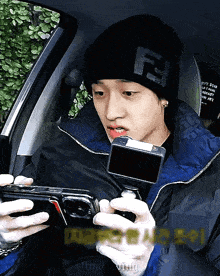 a man wearing a black beanie with the letter f on it is holding a cell phone
