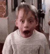 a young boy in a white sweater is making a surprised face .