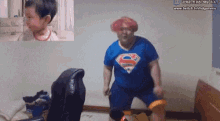 a man in a superman shirt is dancing in front of a screen that says www.twitch.tv/hdgurwins