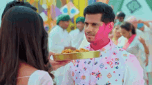 a man with holi paint on his face is holding a tray of food .