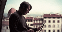 a man is looking at a tablet in front of a window
