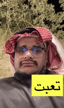 a man wearing glasses and a red and white head scarf has a yellow sign above his head that says ' n '