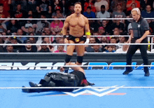 a wrestler is standing in the middle of the ring while another wrestler is laying on the floor