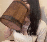 a woman in a white shirt is drinking from a wooden bucket