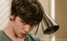 a young man is holding a shower head over his head while wearing a grey shirt .