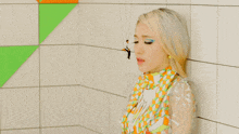 a woman in a colorful dress is leaning against a white tile wall