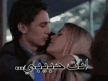 a man and a woman are kissing with arabic writing on the bottom of the image .