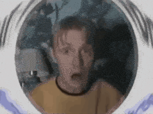 a man in a yellow shirt is looking through a hole in the wall