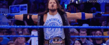 a wrestler is standing in a wrestling ring with his arms outstretched in front of a crowd .