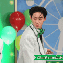 a man in a green bow tie is holding a lollipop in front of balloons and a sign that says #grabfood