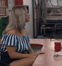 a woman in a striped off the shoulder top is sitting at a table with her legs crossed .