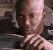 a bald man with a beard is driving a car and looking at the camera