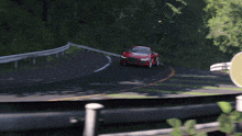 a red car is driving down a road behind a green object