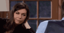 a woman is sitting at a table with a man and holding her head .