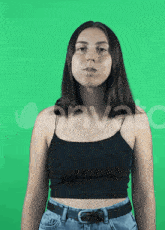 a woman in a black tank top and blue jeans is standing in front of a green screen
