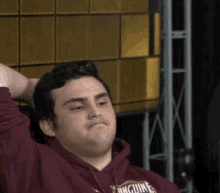 a man wearing a burgundy anguine sweatshirt holds his head