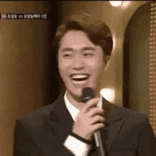 a man in a suit is laughing while holding a microphone .