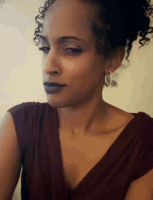 a woman with curly hair wearing a burgundy top and silver hoop earrings