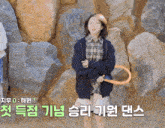 a girl in a plaid shirt is standing in front of a wall of rocks with korean writing on it
