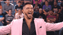 a man wearing glasses and a pink jacket stands in front of a crowd with the hashtag thekamdreesen