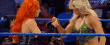 two women are shaking hands in a wrestling ring while a crowd watches .