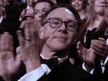 a man in a tuxedo and bow tie applauds in a crowd