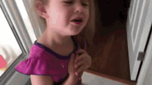 a little girl in a purple dress is crying and holding her chest .