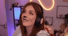 a woman with cat makeup on her face and headphones is sitting in front of a computer screen .