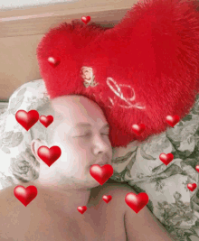 a man laying on a bed with a heart shaped pillow on top of his head