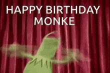 kermit the frog is dancing on a stage in front of a red curtain .