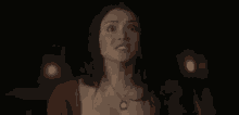 a woman is standing in the dark wearing a necklace and looking at the camera .