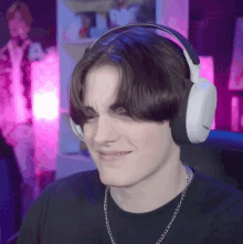 a young man wearing headphones and a chain making a face