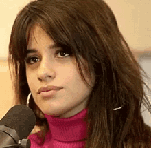 a close up of a woman wearing a pink turtleneck sweater and earrings standing in front of a microphone .