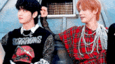 two young men are standing next to each other and one of them is wearing a scorpions shirt .