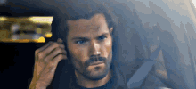 a man with a beard is sitting in a car and talking on a cell phone