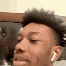 a young man wearing ear buds is making a funny face while sitting on a bed .