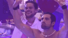 two men are standing next to each other with their arms in the air in a dark room .