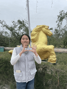 a girl making a heart shape with her hands in front of a gold horse statue