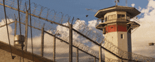 a prison tower behind a barbed wire fence with birds flying around it