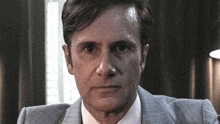 a man in a suit and tie is sitting in front of a window