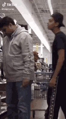 two men are standing next to each other in a store . one is wearing a tommy hilfiger hoodie .