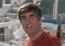 a man with a red shirt on is making a funny face while standing in front of boats .