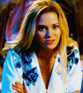 a blonde woman wearing a white shirt with blue flowers on the sleeves